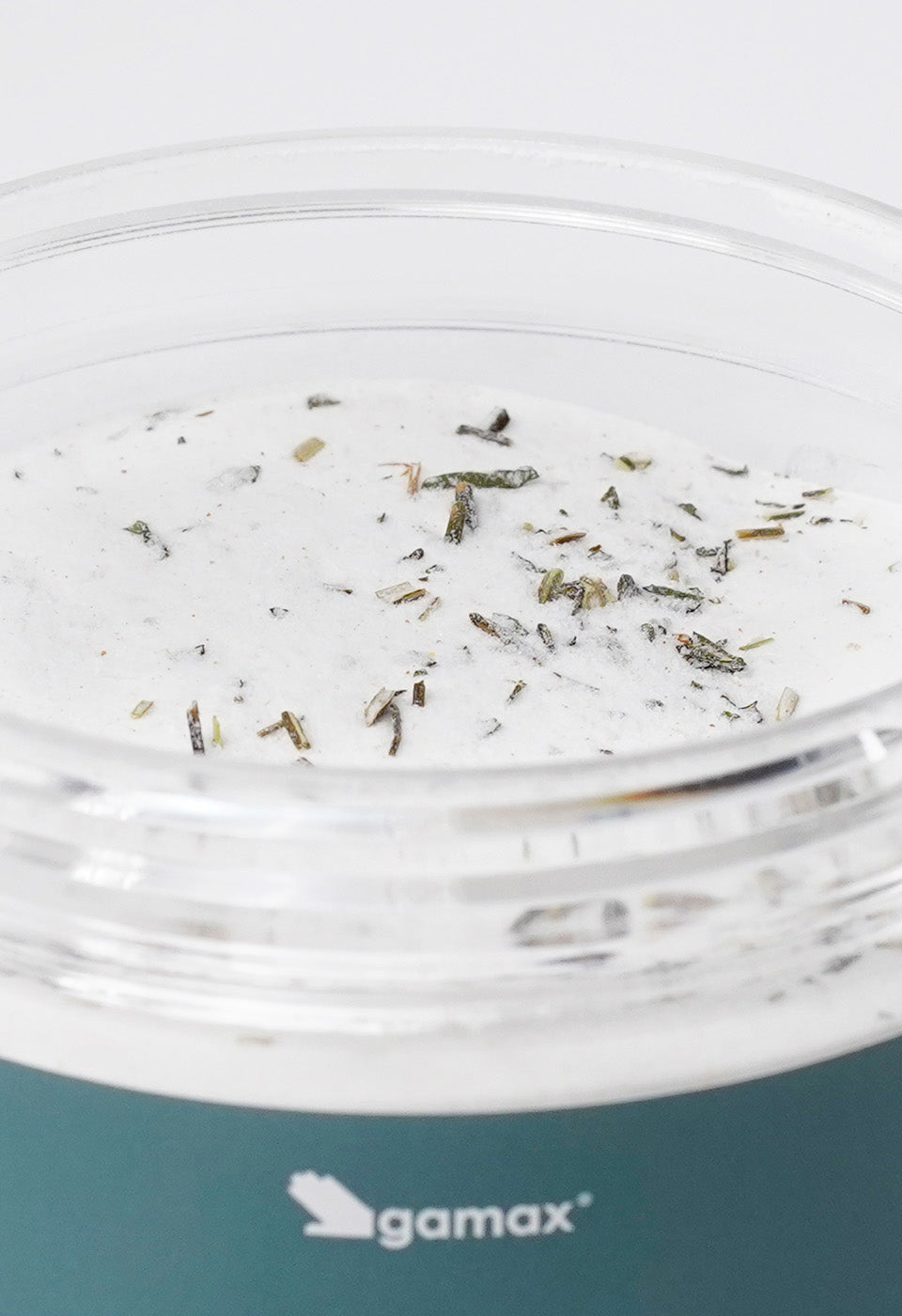 Dettaglio della texture del prodotto Gamax: polvere bianca granulosa con foglie essiccate di menta piperita all'interno.