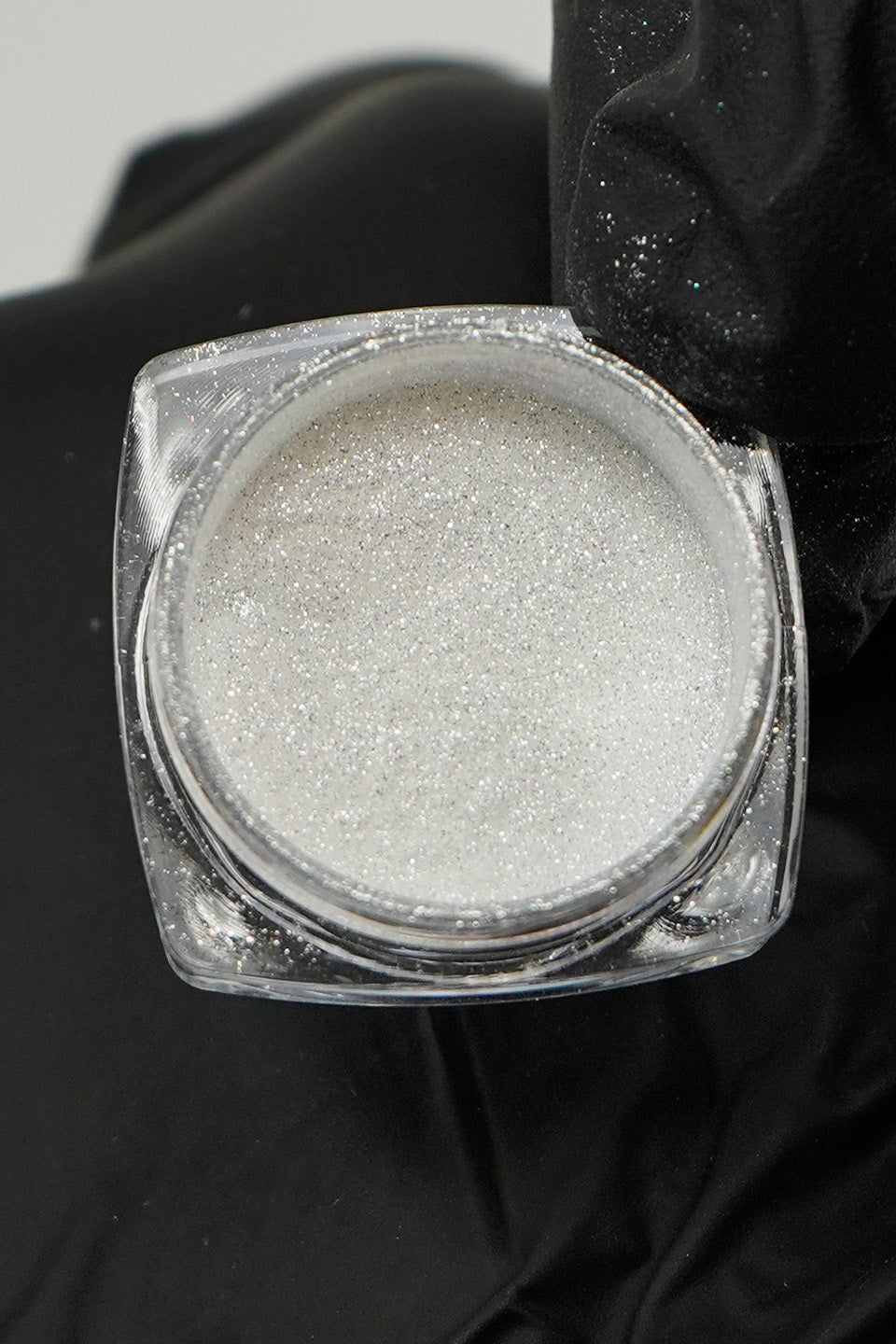 Flacone di polvere per unghie argento cromato aperto, poggiato su un guanto nero.