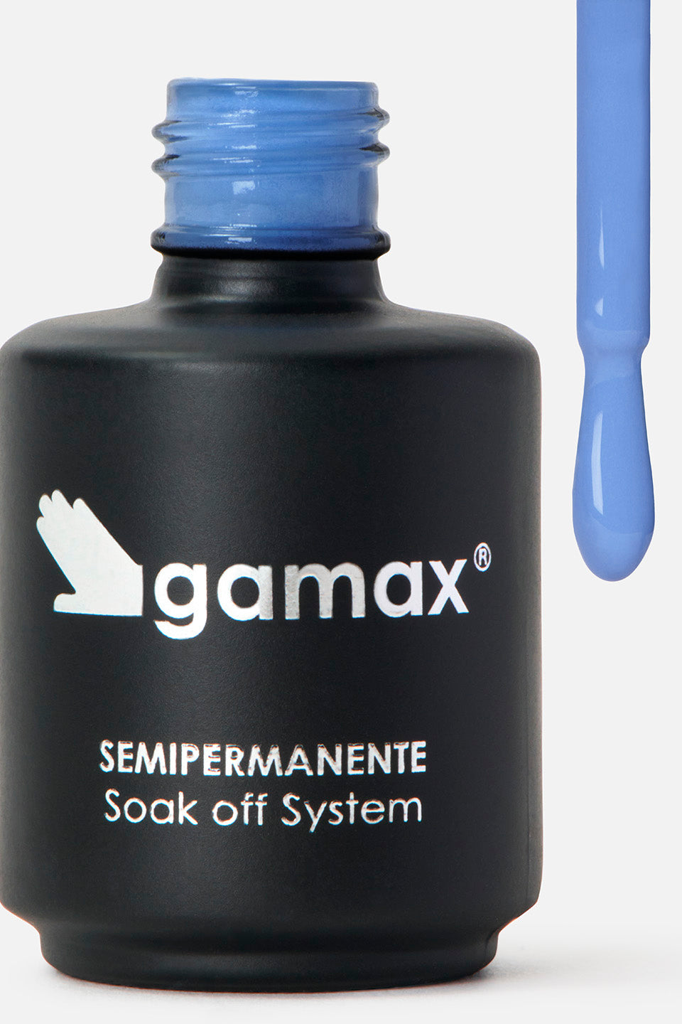 Primo piano di un flacone di smalto nero opaco del marchio Gamax, con scritte bianche che riportano "SEMIPERMANENTE Soak off System". Sulla destra, l'applicatore è sollevato e mostra l'estremità del pennellino coperta da uno smalto fluido di colore blu pastello, con una goccia pronta a scendere.