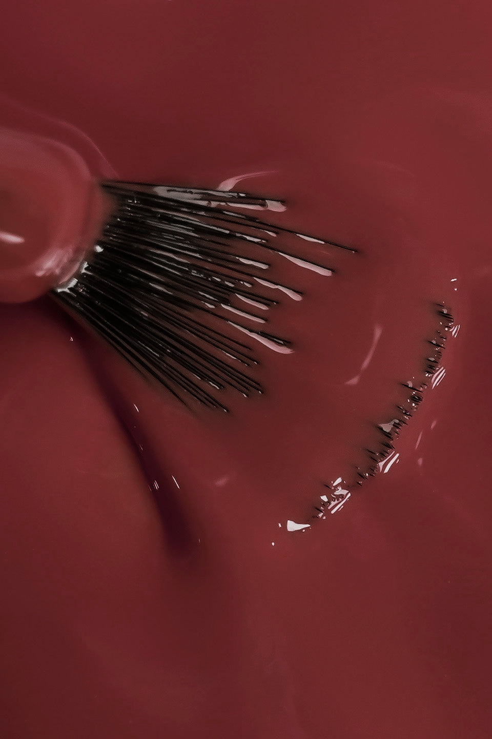 Dettaglio ravvicinato della texture fluida dello smalto semipermanente rosa scuro sussurro. Un pennello a ventaglio è immerso nel colore, mostrando la coprenza omogenea e la finitura lucida del prodotto durante la stesura.