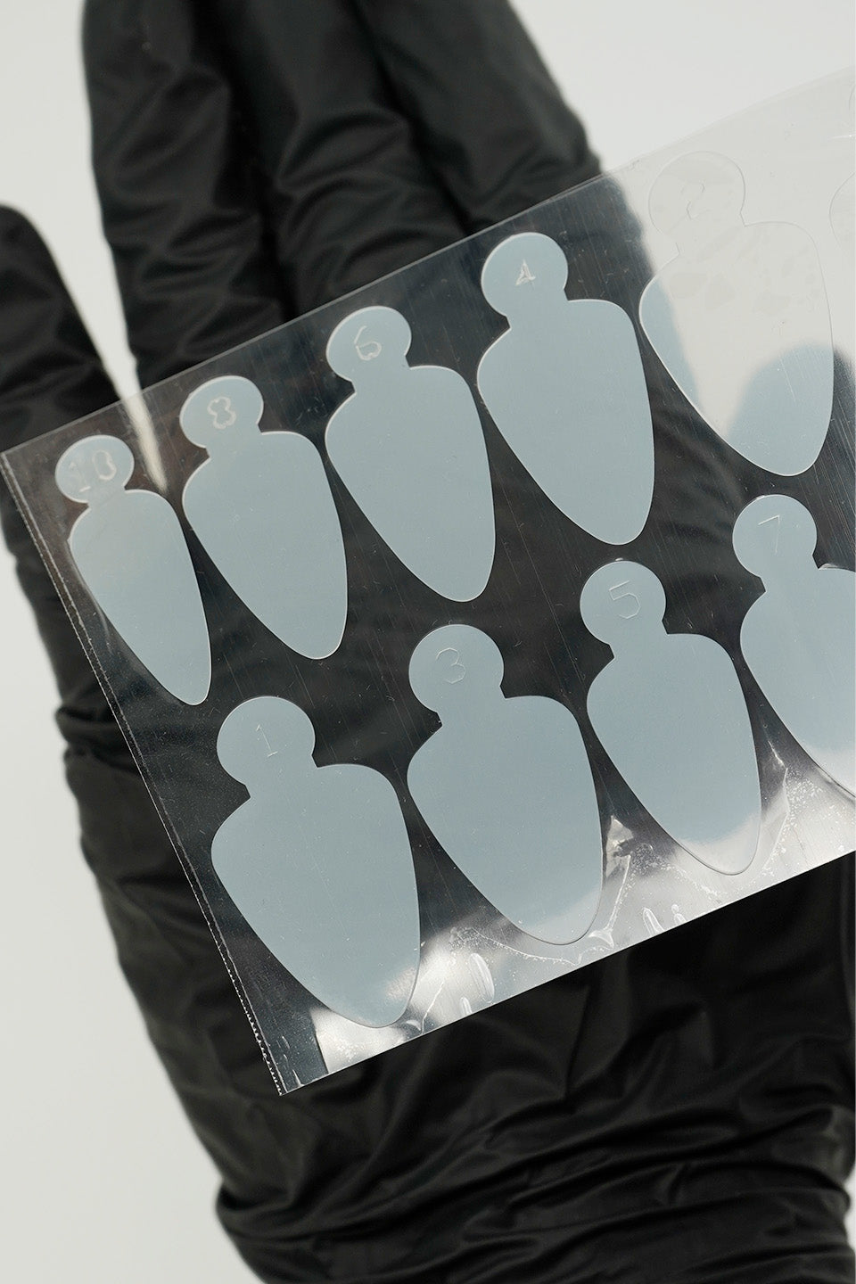 Dettaglio Adesivi in silicone forma j per realizzare unghie dual form in acrygel con. Gli adesivi sono fotografati mentre sono poggiati su un guanto nero per mostrare meglio la forma degli adesivi stessi e per far leggere il numero che corrisponde alla misura.