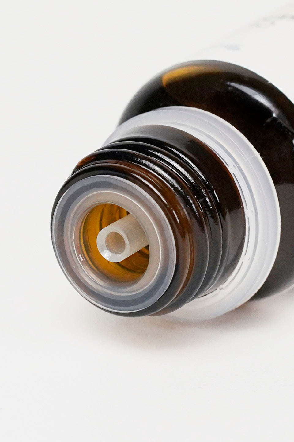 Dettaglio ravvicinato dell'erogatore contagocce in plastica trasparente inserito nel collo di un flacone in vetro scuro con filettatura per il tappo