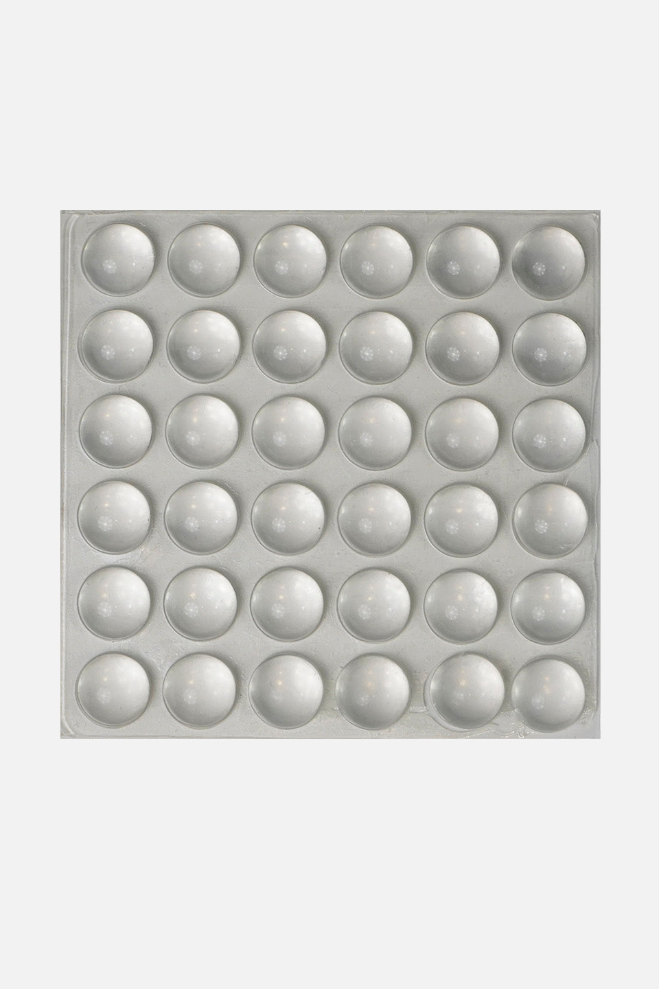 Foglio quadrato contenente 36 bolle adesive in silicone paracolpi sferici e trasparenti per tastiera pc, (disposti in una griglia 6x6) su sfondo grigio chiaro uniforme.