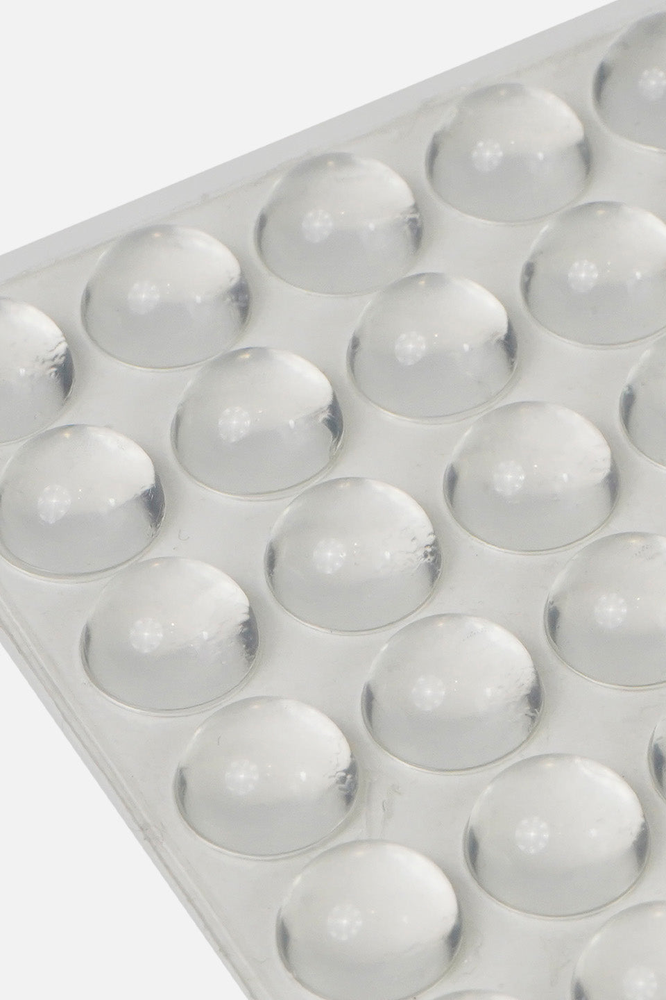 Inquadratura ravvicinata e angolata di un foglio con bolle adesive in silicone paracolpi trasparenti per tastiera pc, che mette in risalto la loro forma a cupola tridimensionale.