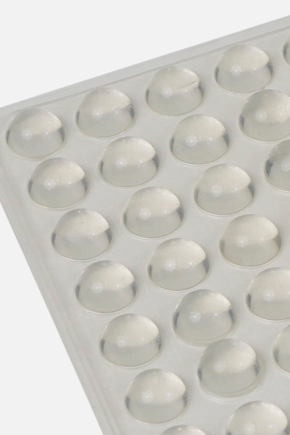 Inquadratura ravvicinata e angolata di un foglio con bolle adesive paracolpi trasparenti per tastiera pc per unghie lunghe, che mette in risalto la loro forma a cupola tridimensionale.