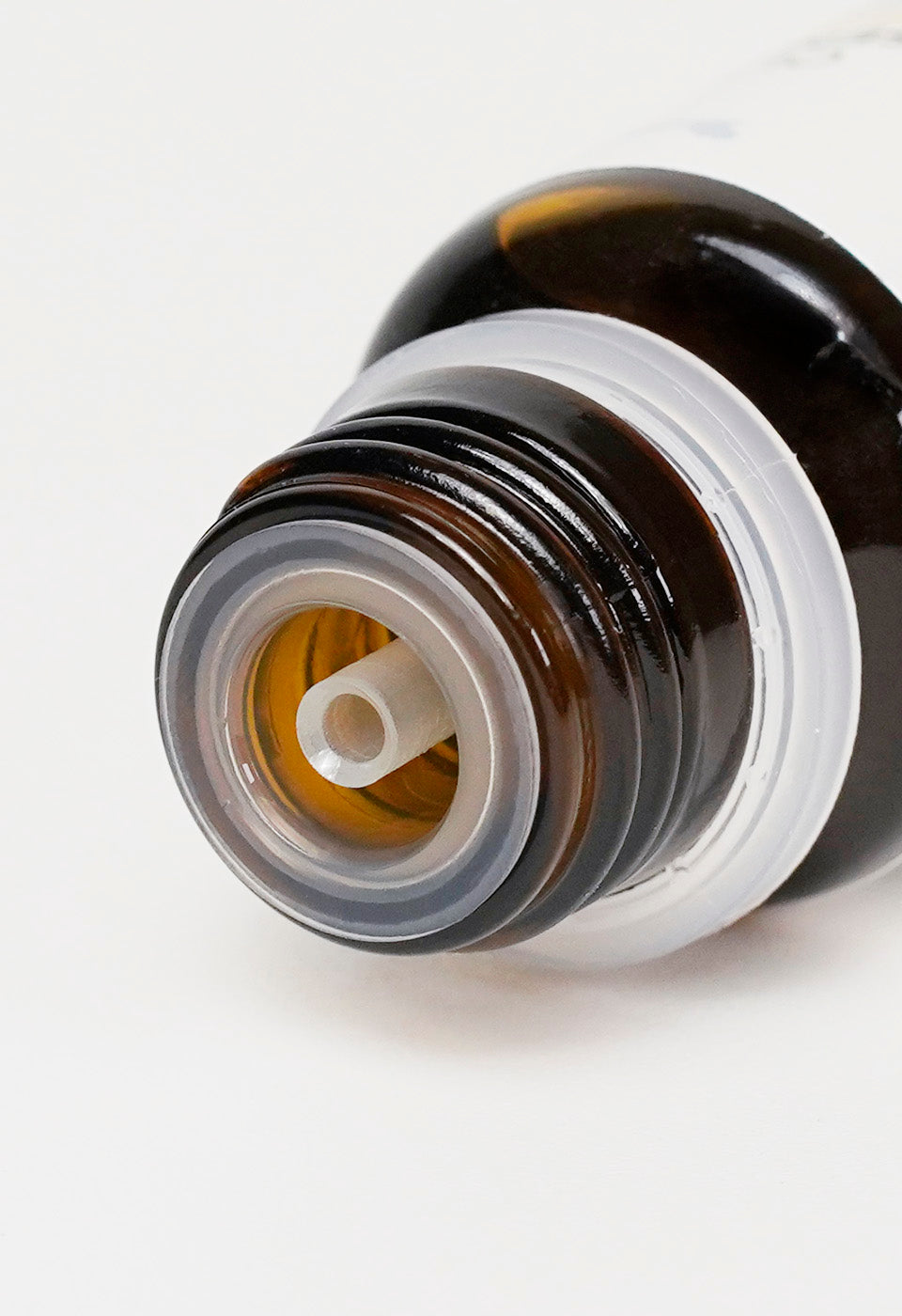 Vista ravvicinata dall'alto dell'imboccatura di un flacone di olio essenziale in vetro scuro, che mostra il dettaglio del riduttore di gocce in plastica trasparente.