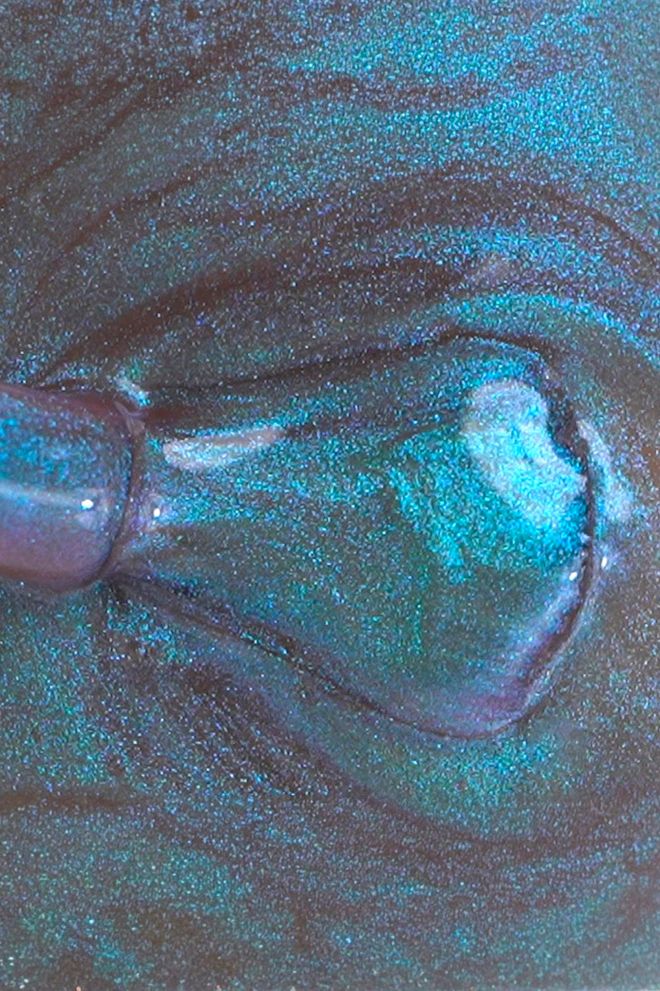 Macro della texture di uno smalto per unghie fluido e scintillante. Il colore è una miscela ipnotica di pigmenti blu petrolio e verde acqua con micro-glitter luminosi e venature viola scuro che creano un effetto galassia o metallizzato multistrato
