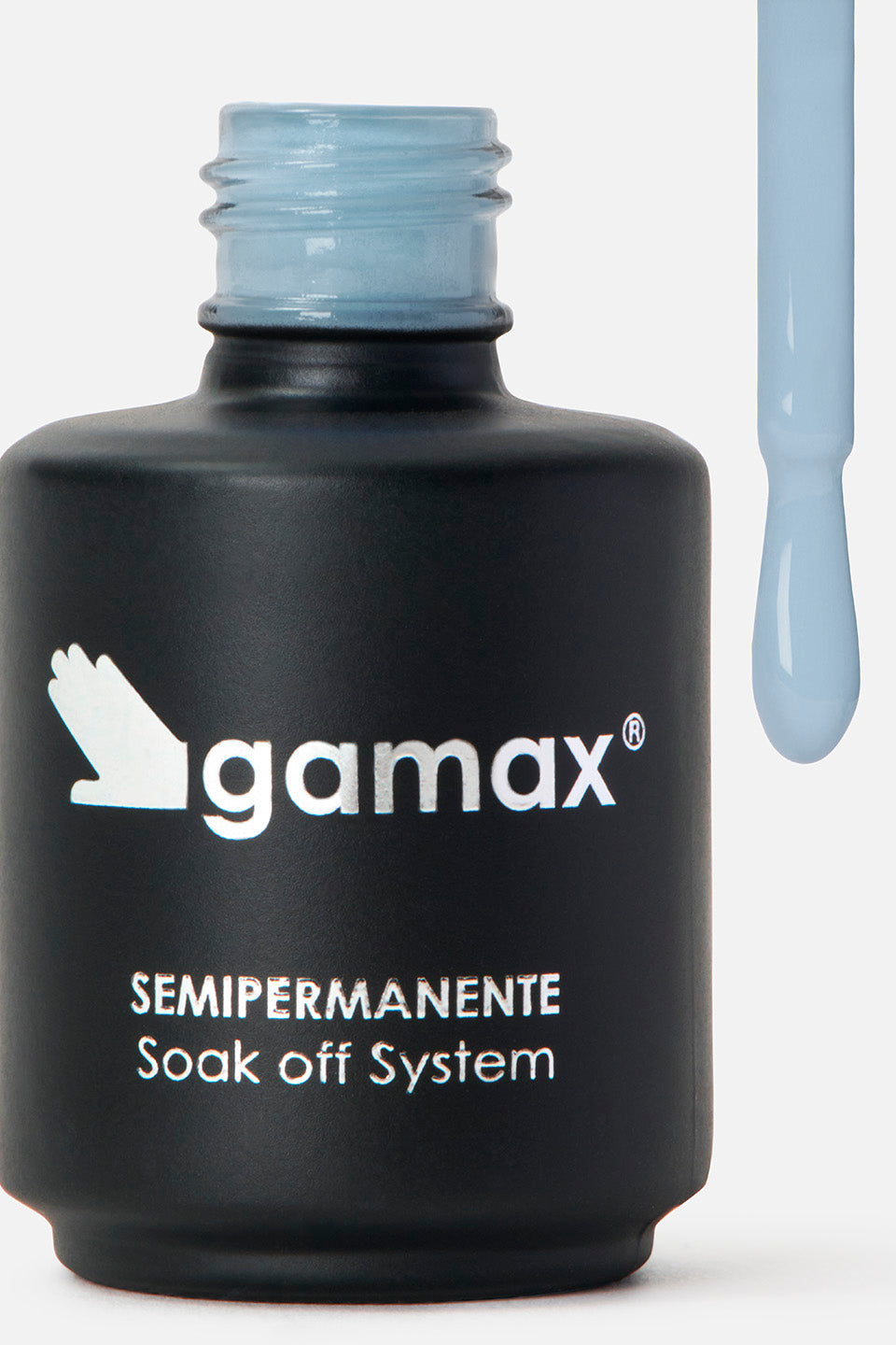 Primo piano di un flacone di smalto nero opaco del marchio Gamax, con scritte bianche che riportano "SEMIPERMANENTE Soak off System". Sulla destra, l'applicatore è sollevato e mostra l'estremità del pennellino coperta da uno smalto fluido di colore azzurro pastello, con una goccia pronta a scendere.