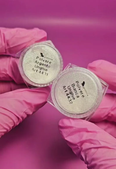 Video tutorial di applicazione delle polveri per unghie bianche e argento. Applicazione su due tip: una nera e una nude per mostrare l'effetto su due diverse colorazioni. L'operatrice indossa guanti rosa, il tutorial viene eseguito su sfondo rosa. 