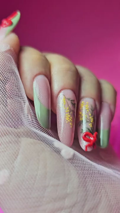 Nail art per la Festa della Donna con decorazioni a mano libera di rami di mimosa gialla su base rosa nude glitterata, French manicure verde pastello e fiocco rosso 3D in rilievo su unghie a mandorla