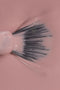 Inquadratura ravvicinata dall'alto che mostra la texture di uno smalto liquido color rosa chiaro. Al centro, le setole nere di un pennellino da stesura sono aperte a ventaglio e parzialmente immerse nel prodotto, evidenziando la consistenza fluida, cremosa e coprente dello smalto.